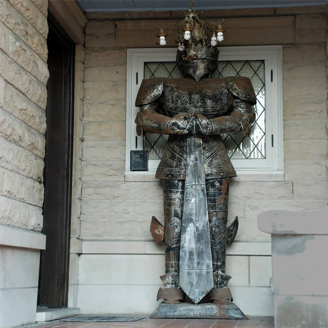 a giagantic metal knight statue stands guard outside a front door